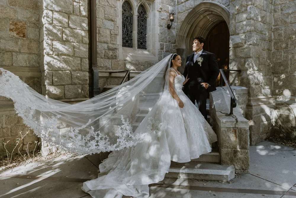 Bride in a ball gown with a long embroidered cathedral veil spread down a set of stone castle steps
