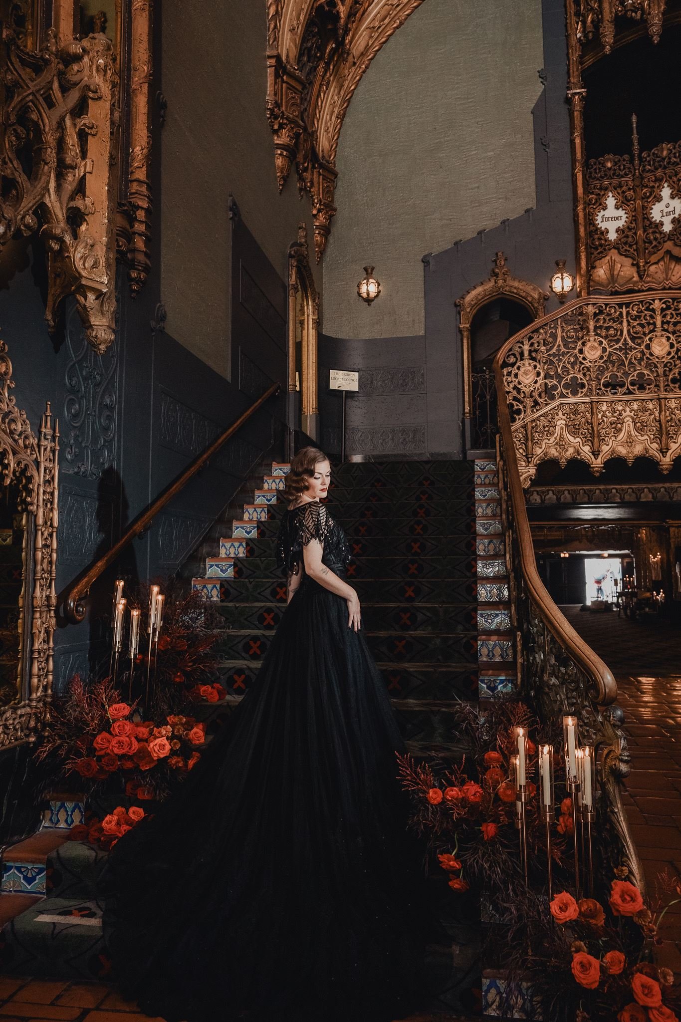 Bride in a black art deco wedding gown with a cathedral train descending the grand staircase of a historic Los Angeles theatre