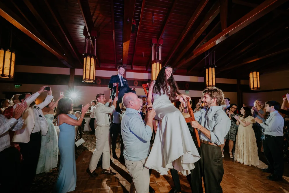 Bride raised on a chair during the hora in a wooden barn reception