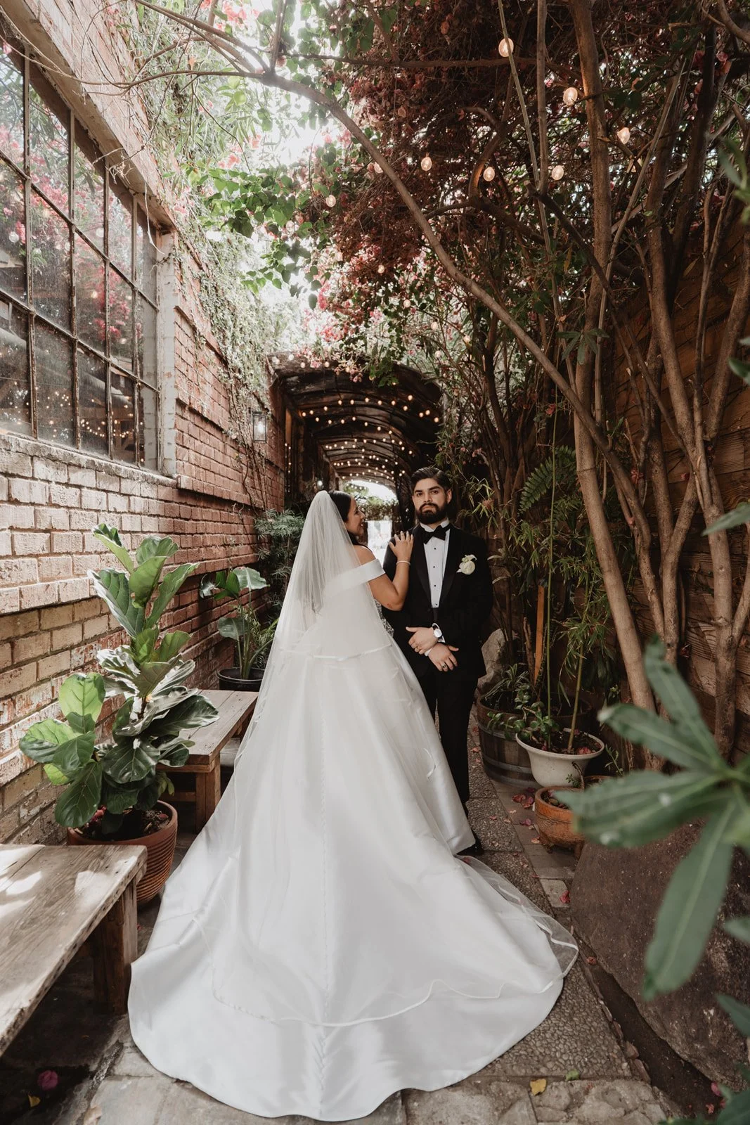 Couple in the leafy brick passage with hanging plants and lights at Seventh Place