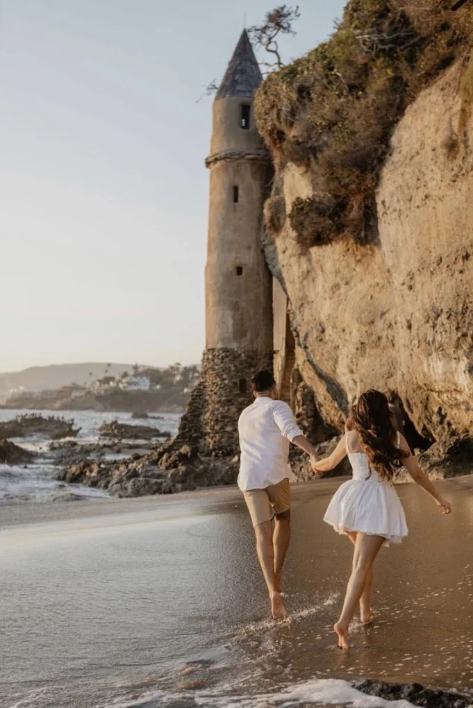 Couple running along the shoreline below a coastal cliff at golden hour