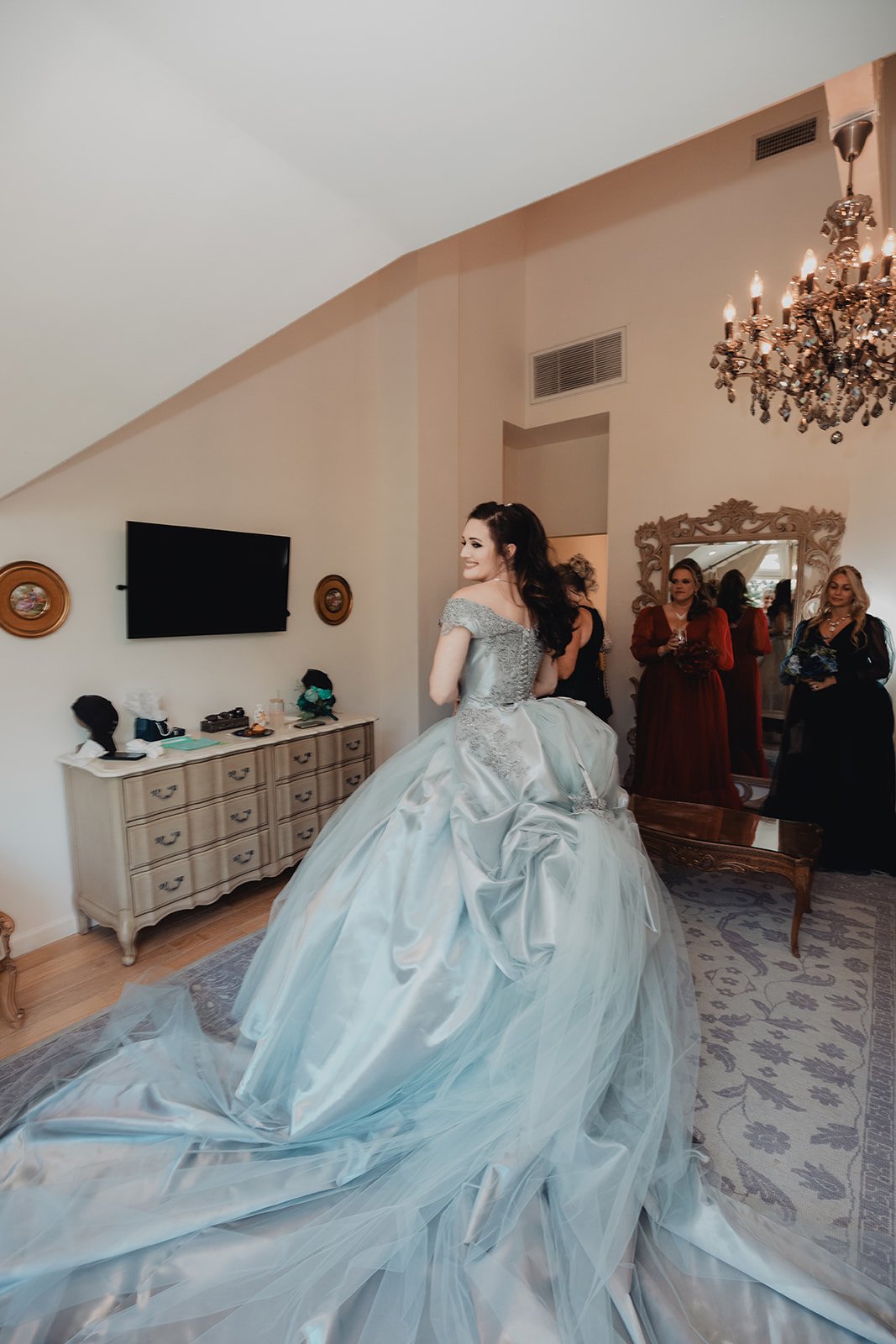 Bride in a pale blue tulle ball gown with a cathedral train, surrounded by her wedding party in a getting-ready suite
