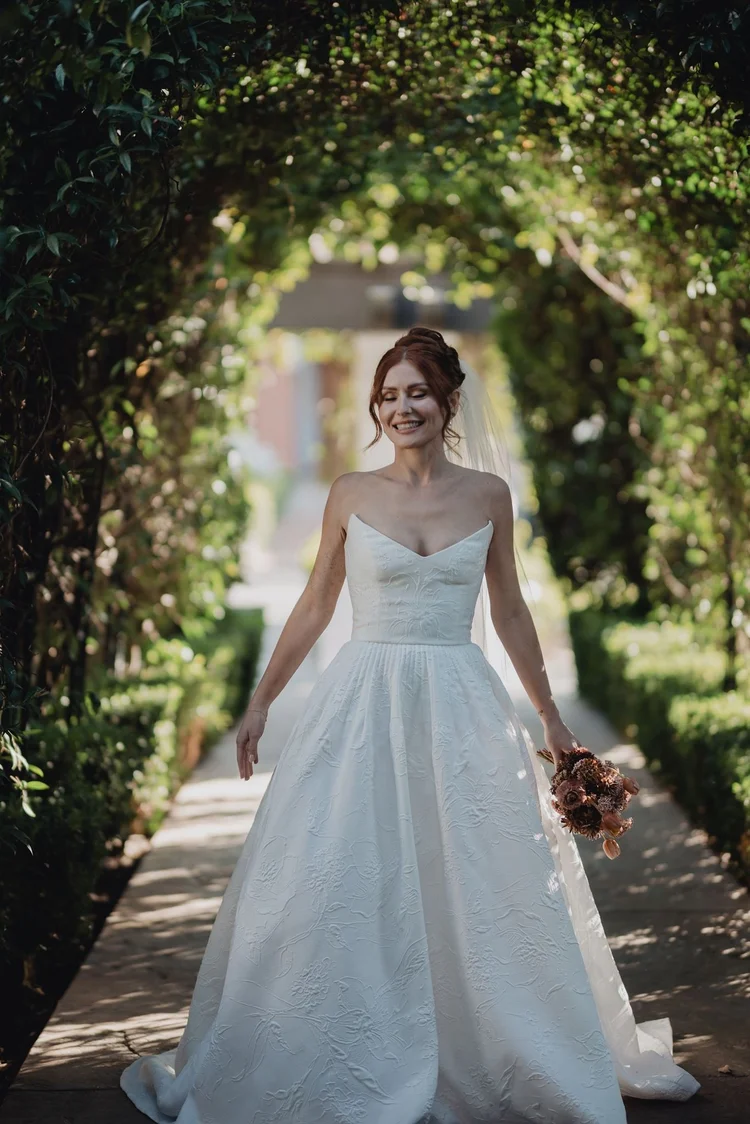 Bride in a simple pleated A-line wedding dress with a court train walking a garden path