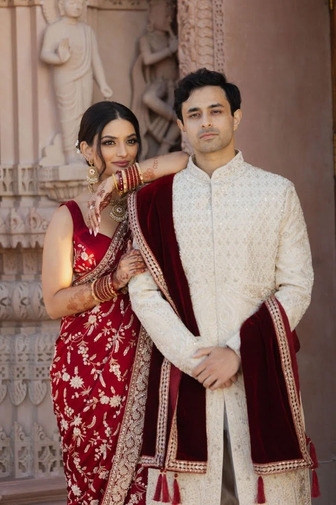 Bride in a red lehenga and groom in an ivory sherwani at the reception