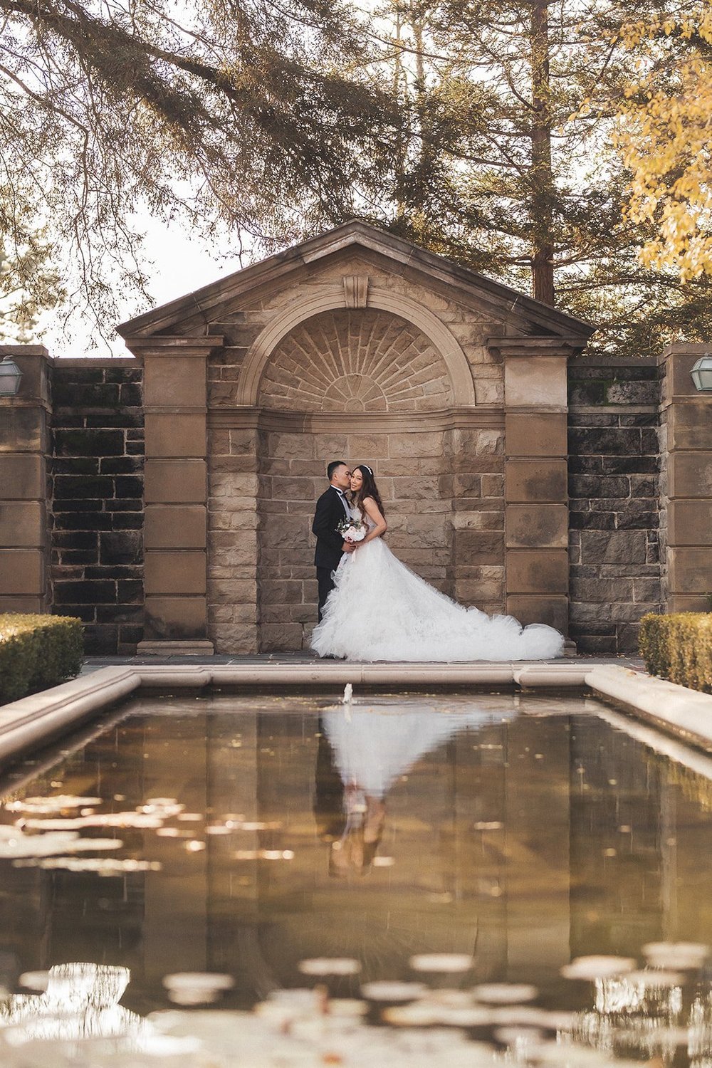 Bride reflected in a fountain pool beside a stone archway at Greystone Mansion in Beverly Hills