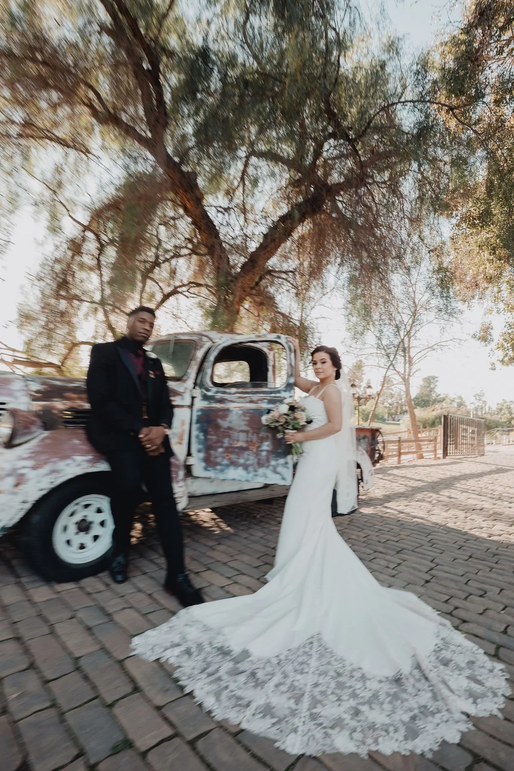 Bride and groom beside a vintage truck under mature oak trees at Lake Oak Meadows in Temecula