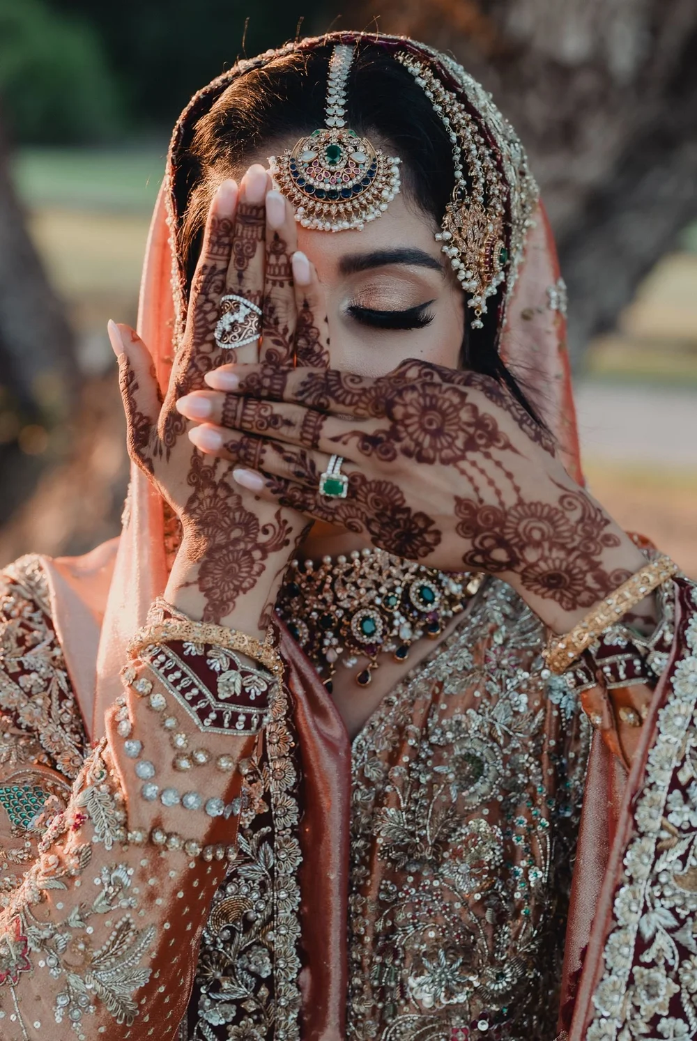 Bride covering her eyes with hennaed hands in the late afternoon light