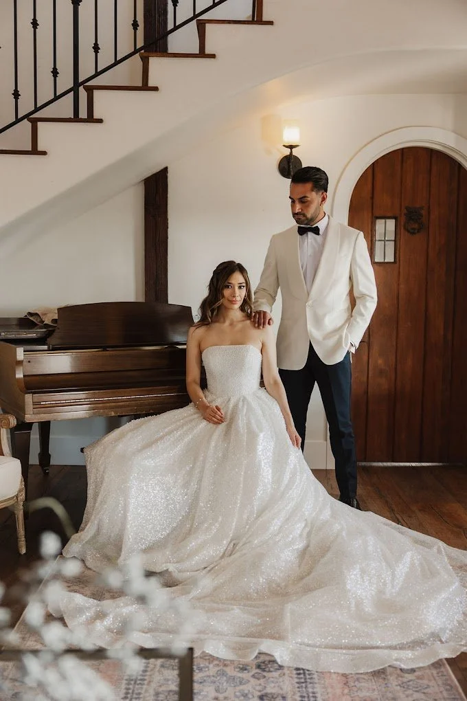 Bride and groom beside a grand piano, her ballgown spread across the floor