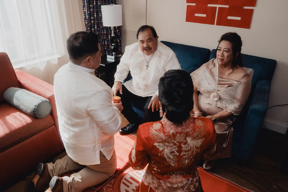 Bride in a red qun kwa kneeling to serve tea to her family at a Chinese tea ceremony