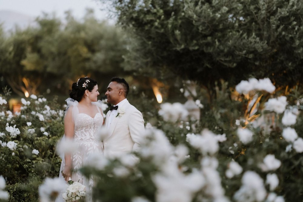 Bride and groom close together among the white roses at Tuscan Rose Ranch