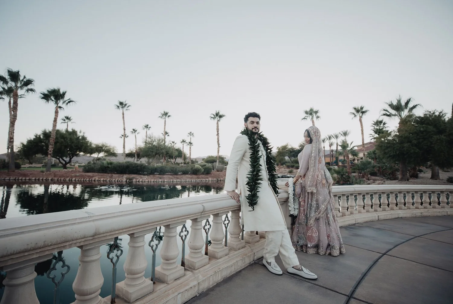 Couple in traditional Pakistani wedding attire on the balustraded terrace above the water at Siena Golf Club