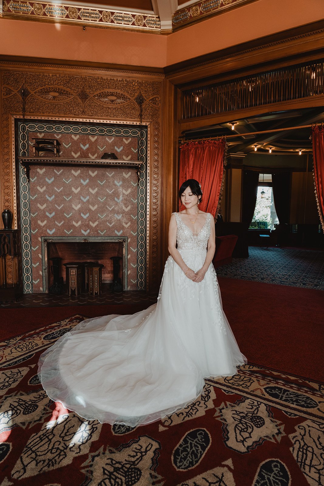 Bride in an A-line lace gown with a chapel train spread across a patterned carpet in an ornate historic ballroom
