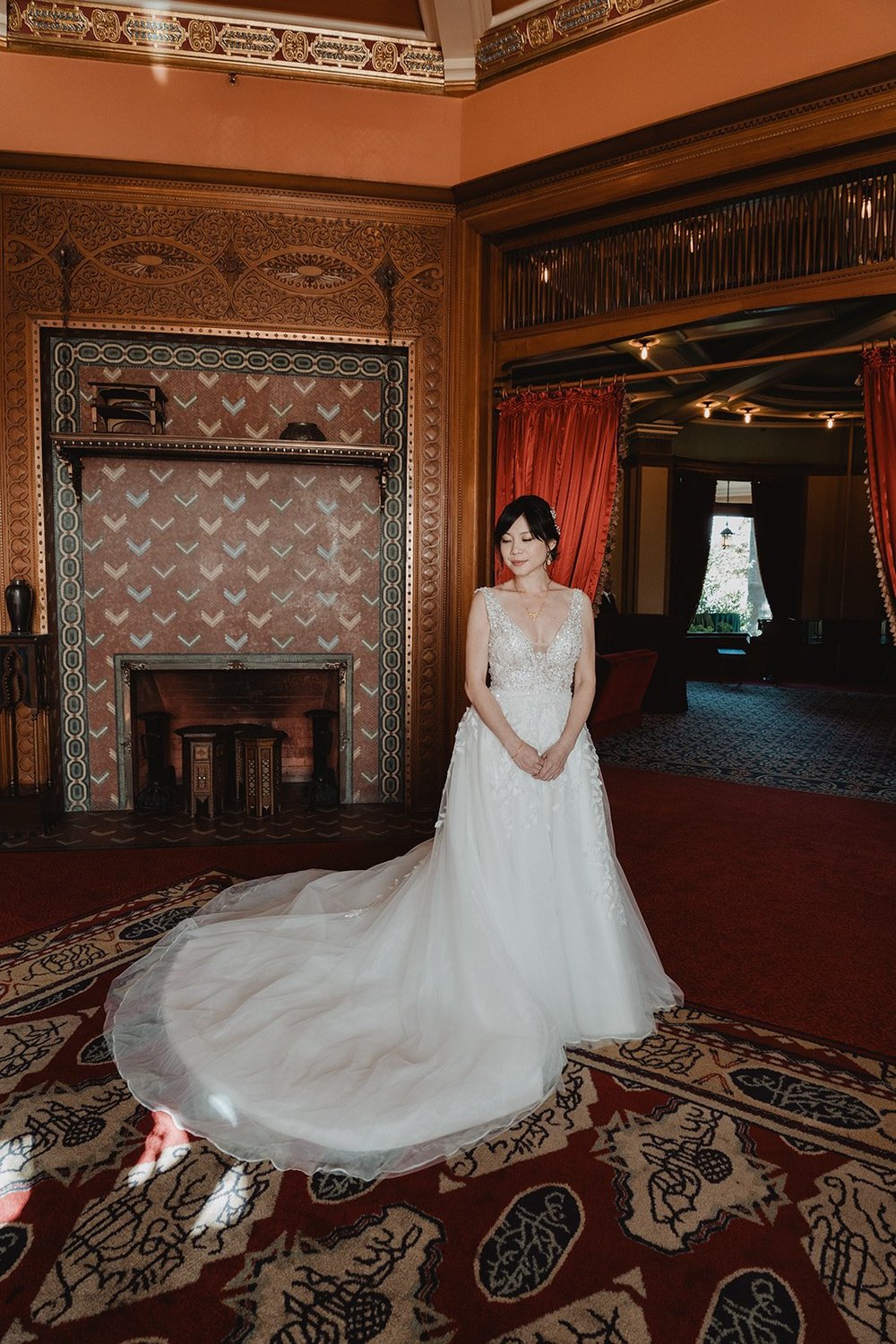Bride in an A-line lace gown with a full tulle overskirt spread across the patterned floor of a historic ballroom