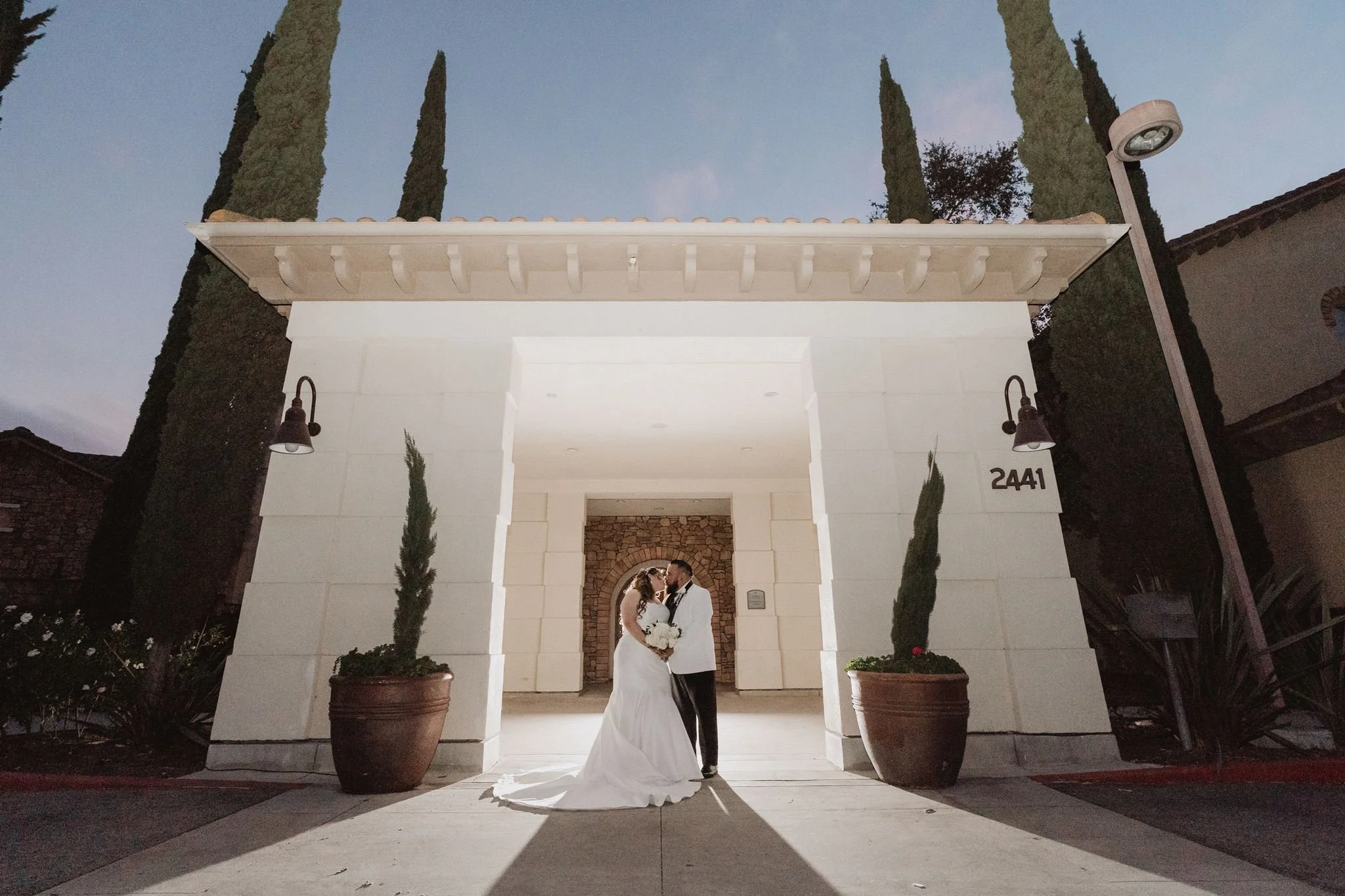 The lit stone entry flanked by cypress trees and terracotta pots at Vellano Estate in Chino Hills