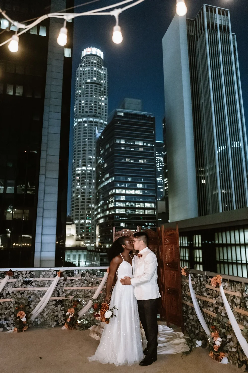Night portrait on the rooftop terrace with the downtown Los Angeles skyline lit behind the couple
