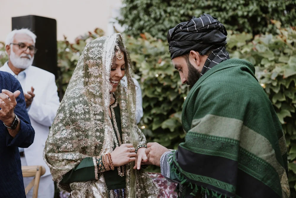 Groom placing the ring on the bride as family look on at an Afghan and Pakistani wedding