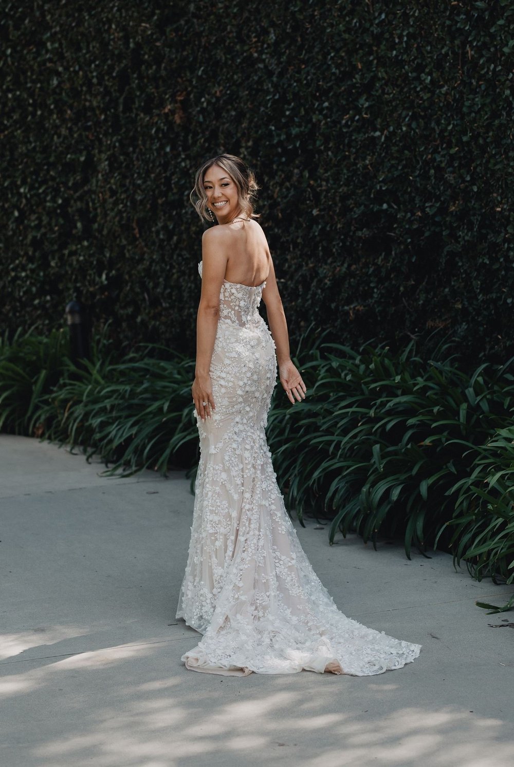 Back detail of a floral appliqué fit-and-flare wedding dress against a wall of green ivy