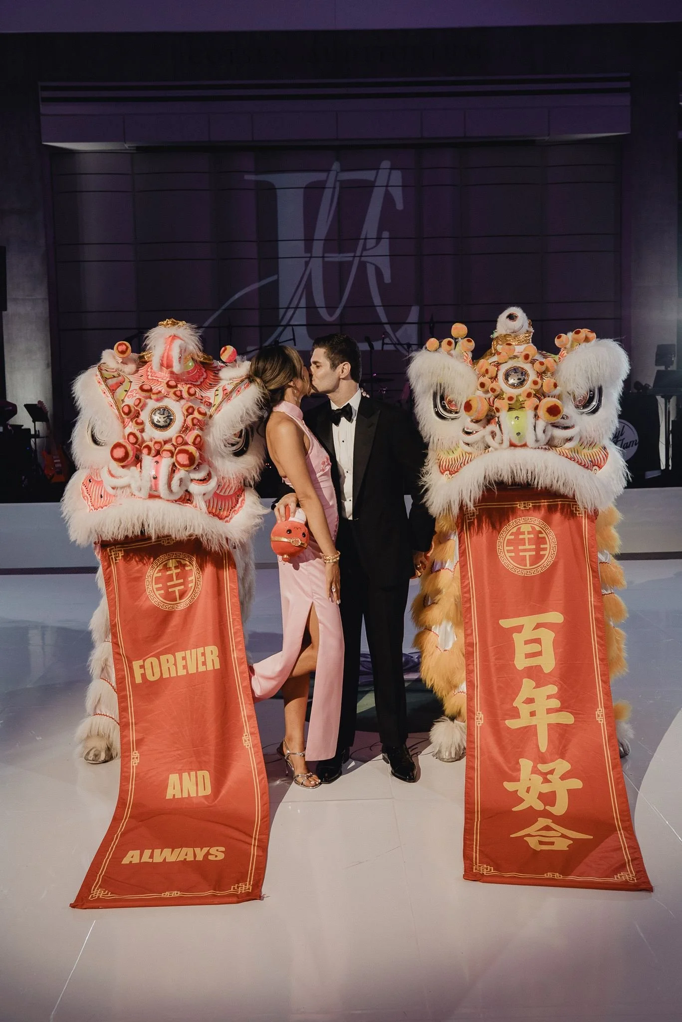 Bride and groom standing between two lions in front of a banner reading a hundred years of happy union