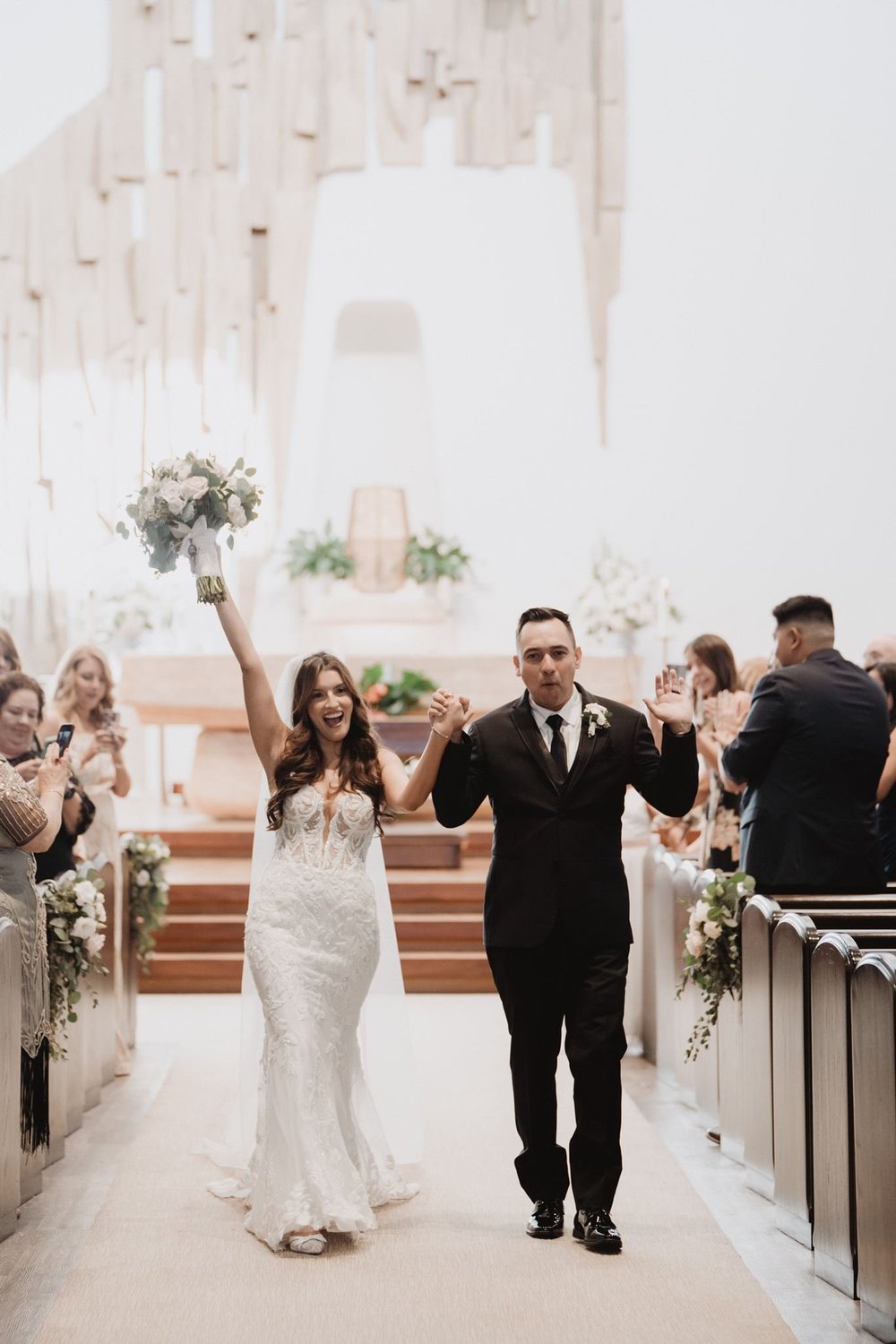 Bride in a deep-V lace mermaid gown celebrating with her husband during the recessional