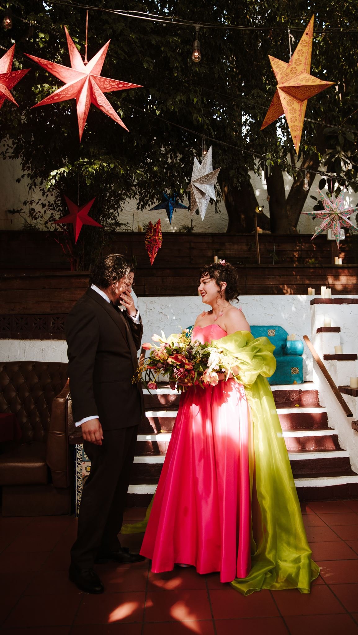 Bride in a hot pink and chartreuse gown descending steps with her father beneath red and gold paper star lanterns