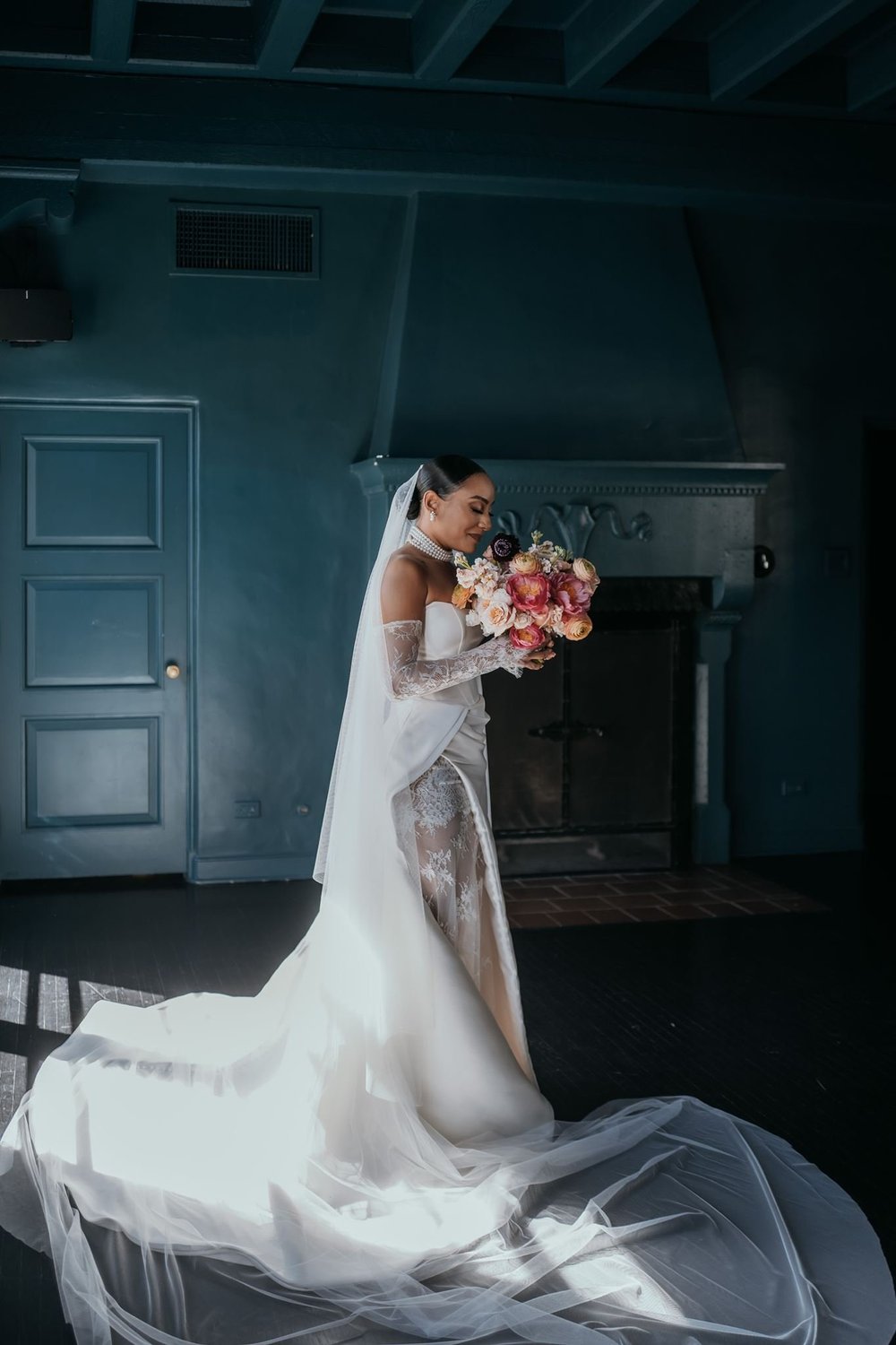 Bride in a fitted ivory gown with a detachable chapel train and long lace-edged veil in a dark green panelled room