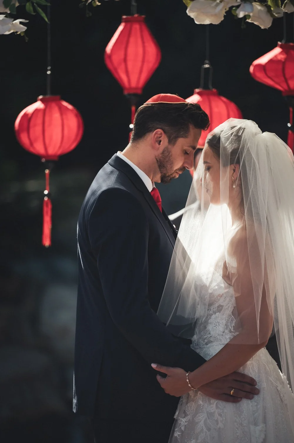 Couple beneath red paper lanterns at a Chinese and Jewish wedding in Los Angeles