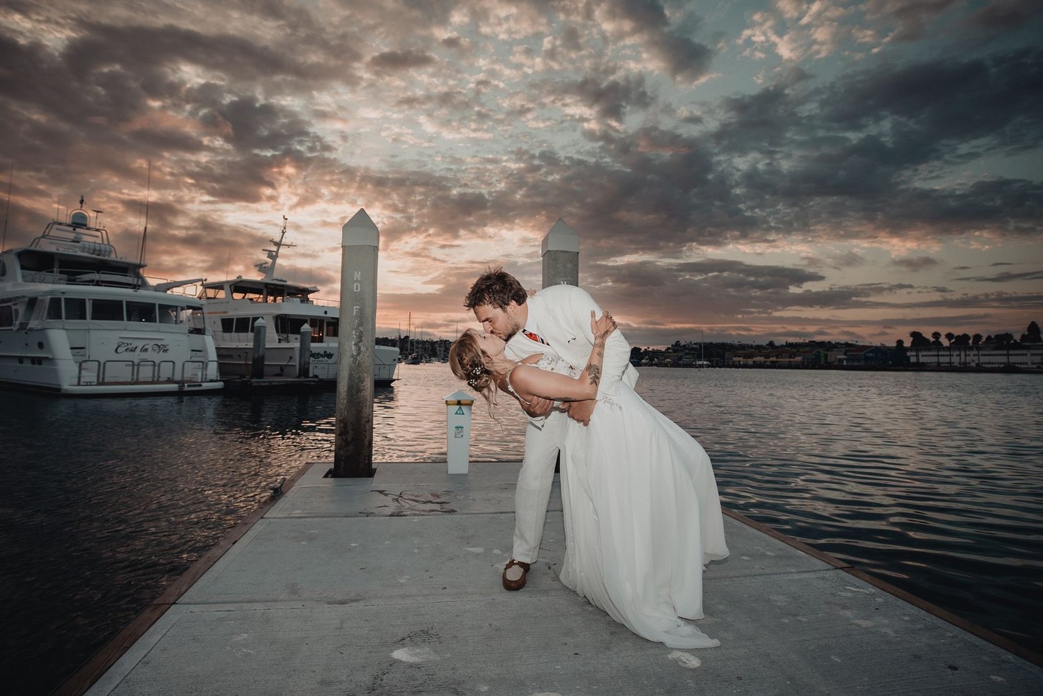Couple dipping at sunset on the Bali Hai dock, yachts moored alongside and the San Diego skyline across the bay