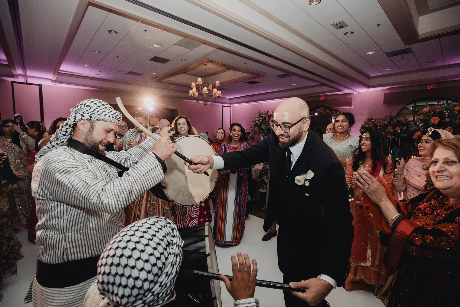 Zaffa drummers in striped robes and keffiyehs leading the groom through a crowded ballroom