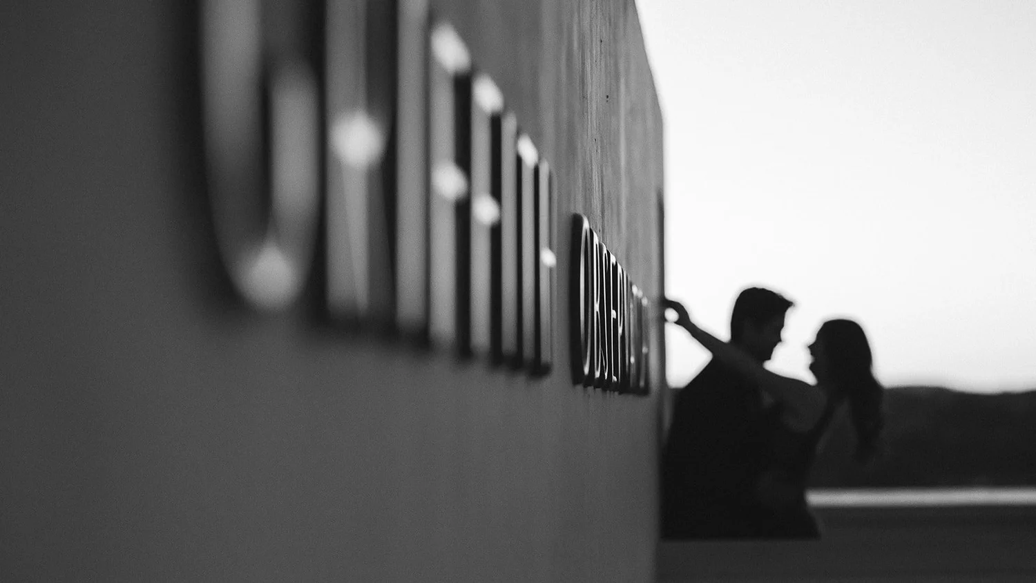Silhouette of a couple beyond the Observatory wall at sunset, the row of exterior lamps running away from the camera