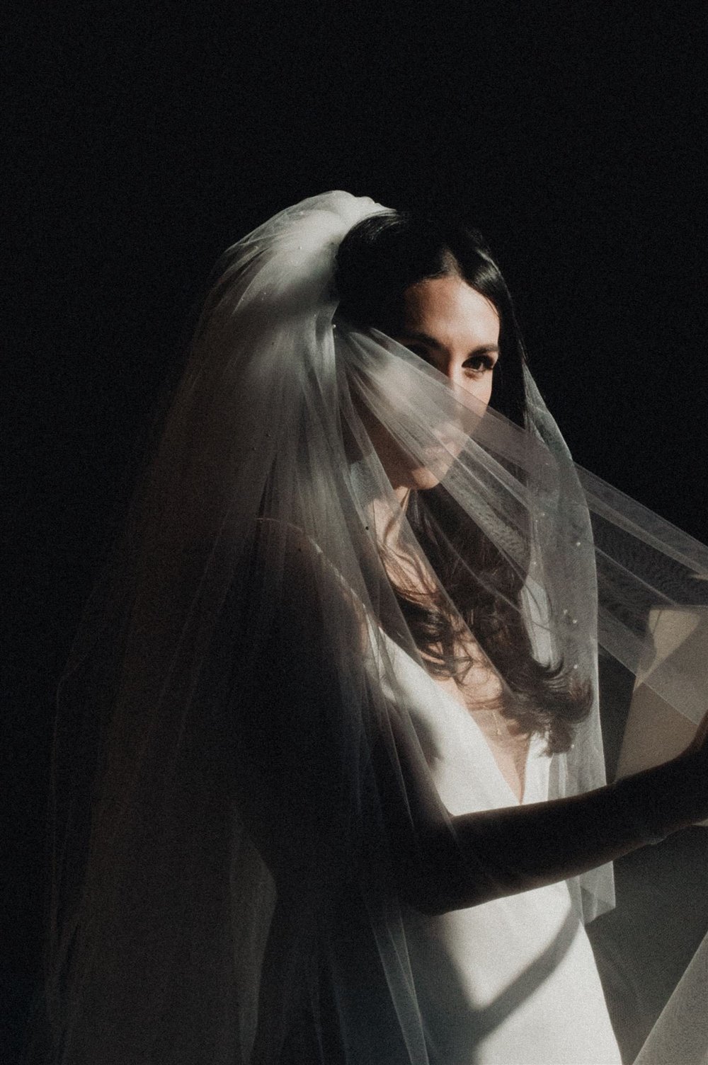 Bride under a pearl-edged veil at Rosewood Miramar Beach, lit by hard directional light against a dark ground
