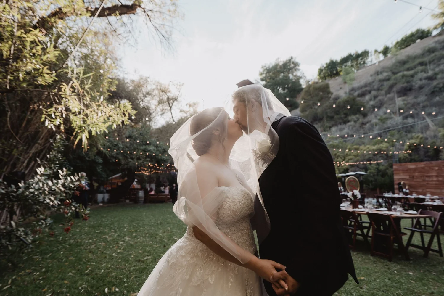 Veil blowing across the couple on the garden lawn at The 1909, with reception tables and string lights beyond