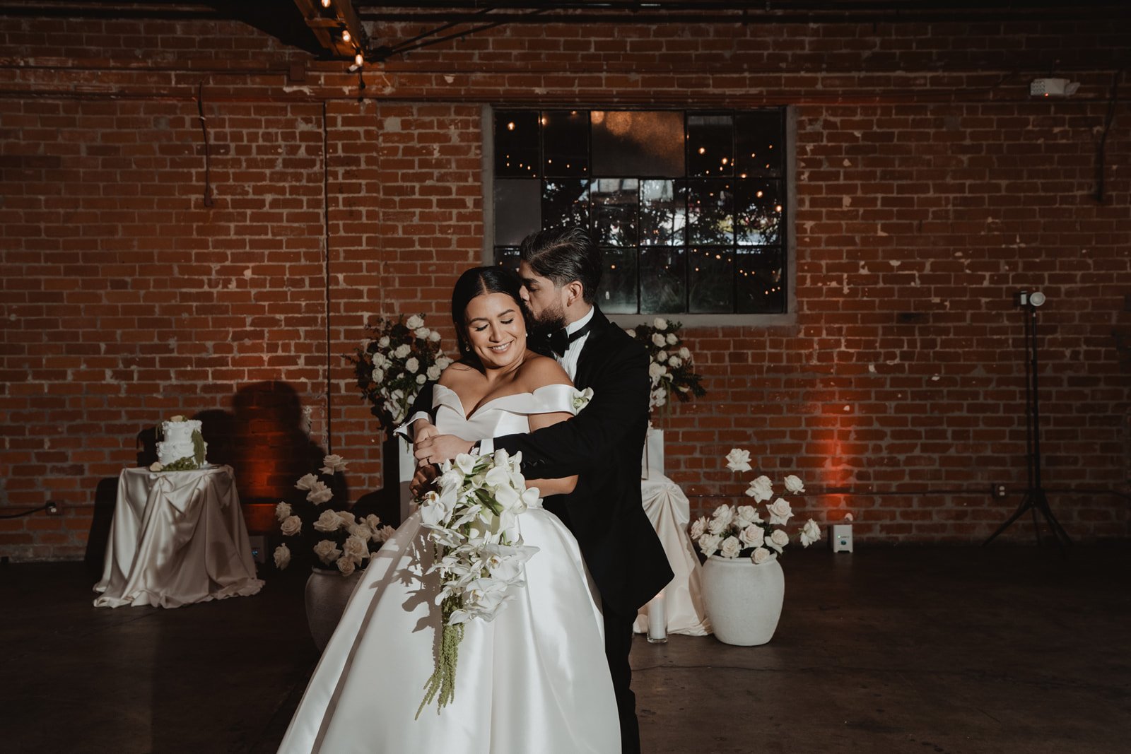 Couple embracing in the red-brick room with candles and white flowers at Seventh Place in downtown Los Angeles