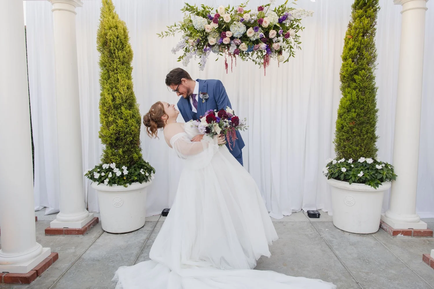 Groom dipping the bride in front of a white floral backdrop between columns at Five Crowns