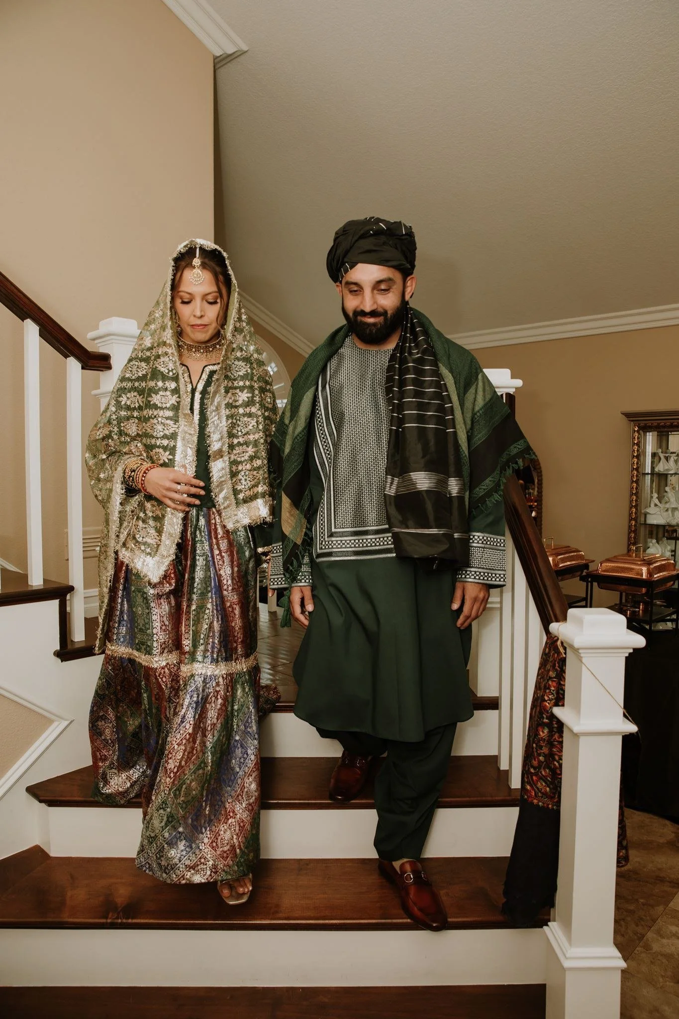 Couple in traditional Afghan attire walking down the staircase of the family home