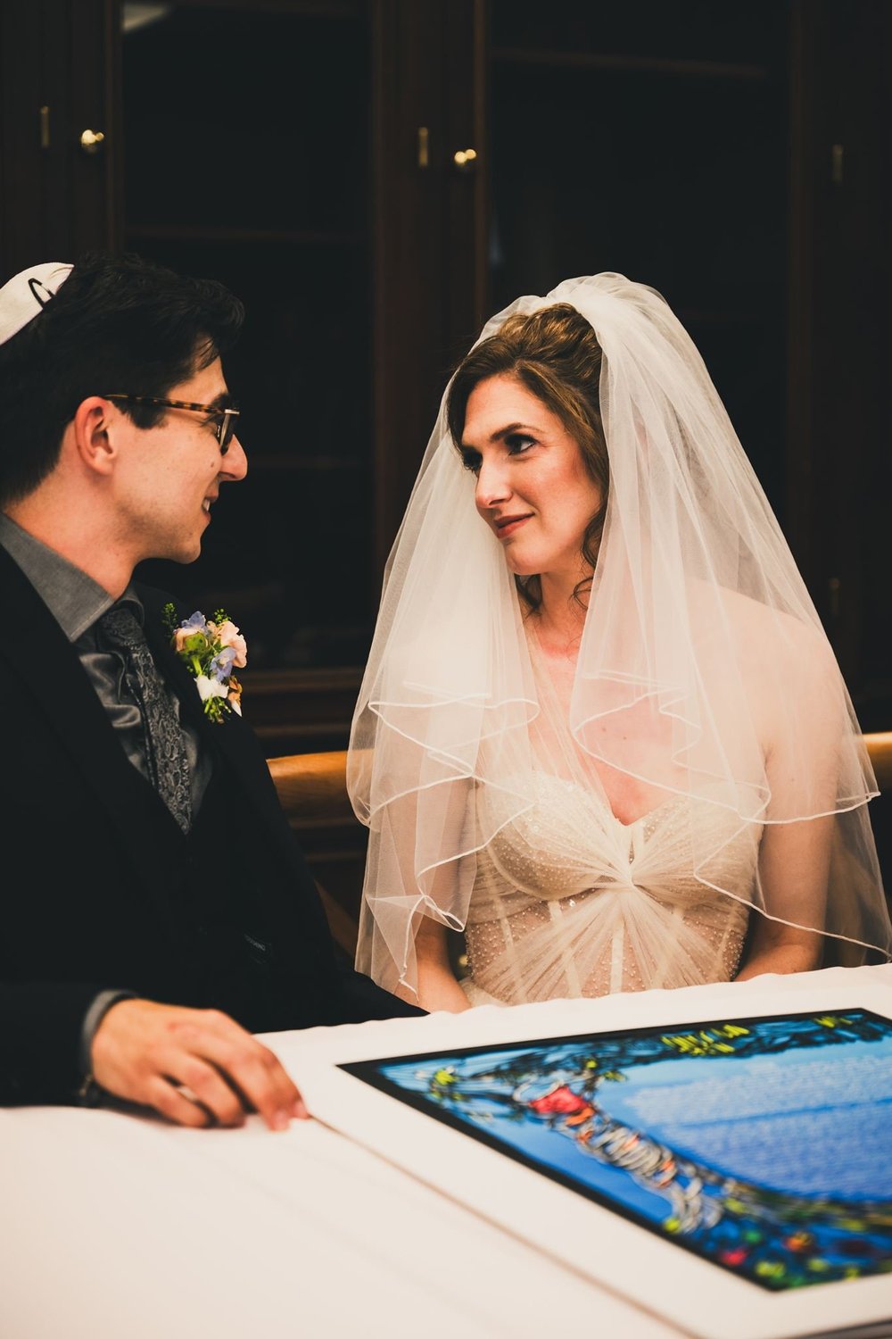 Bride in her veil seated at the ketubah table as the document is prepared