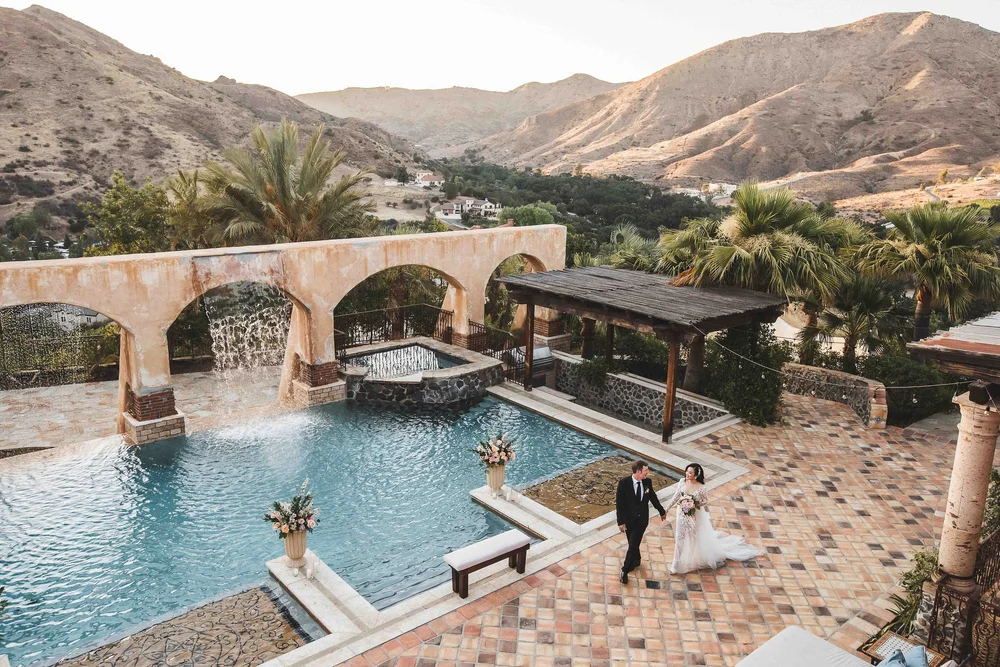 Couple walking beside the pool and stone aqueduct at Villa de la Vina, mountains in the background