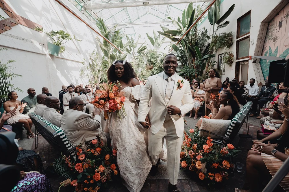 Bride and groom walking back down the aisle after their ceremony at Valentine DTLA, rust and orange florals lining the greenhouse