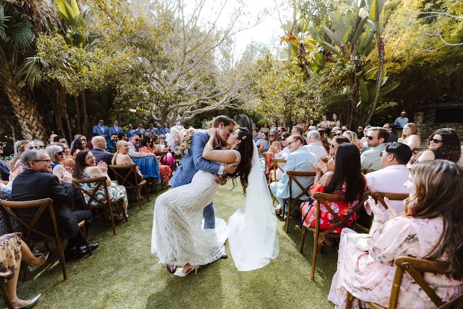 Wedding ceremony on a turf aisle at Botanica in Oceanside, guests seated beneath dense subtropical planting