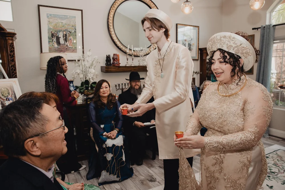 Couple in ao dai serving tea to seated elders during the Vietnamese tea ceremony
