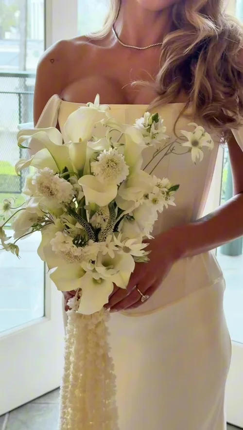 A bride holding a white calla lily bouquet against her gown, filmed close on a phone