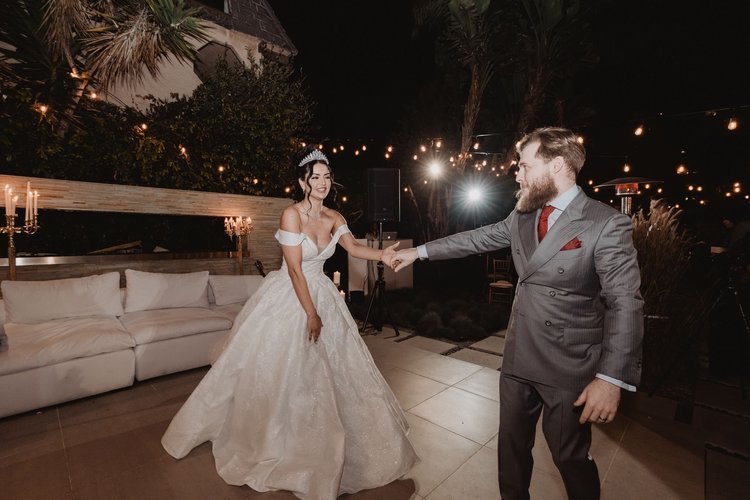 Bride in an off-the-shoulder ball gown reaching for her husband at a candlelit evening reception