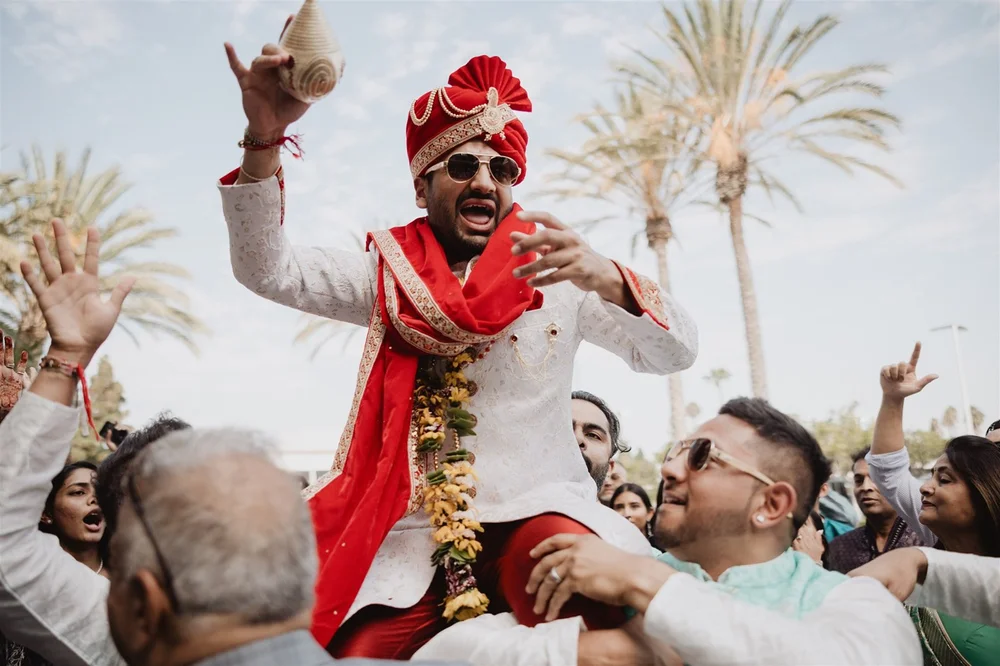 Groom in a cream sherwani and red safa lifted on shoulders during the baraat at the Hyatt Regency Huntington Beach