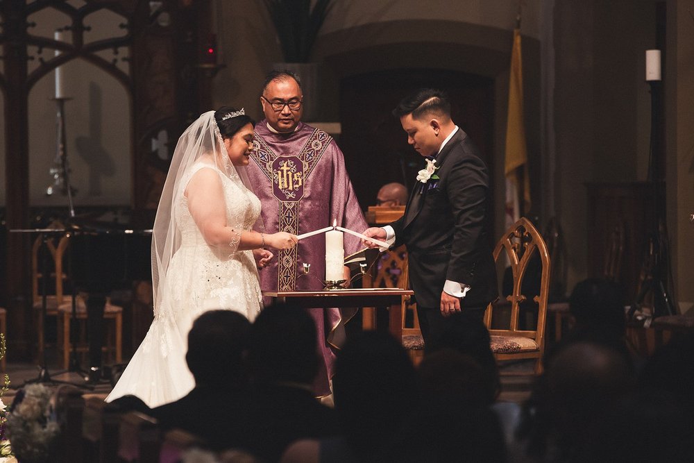 Couple lighting the unity candle with the priest during a church wedding ceremony