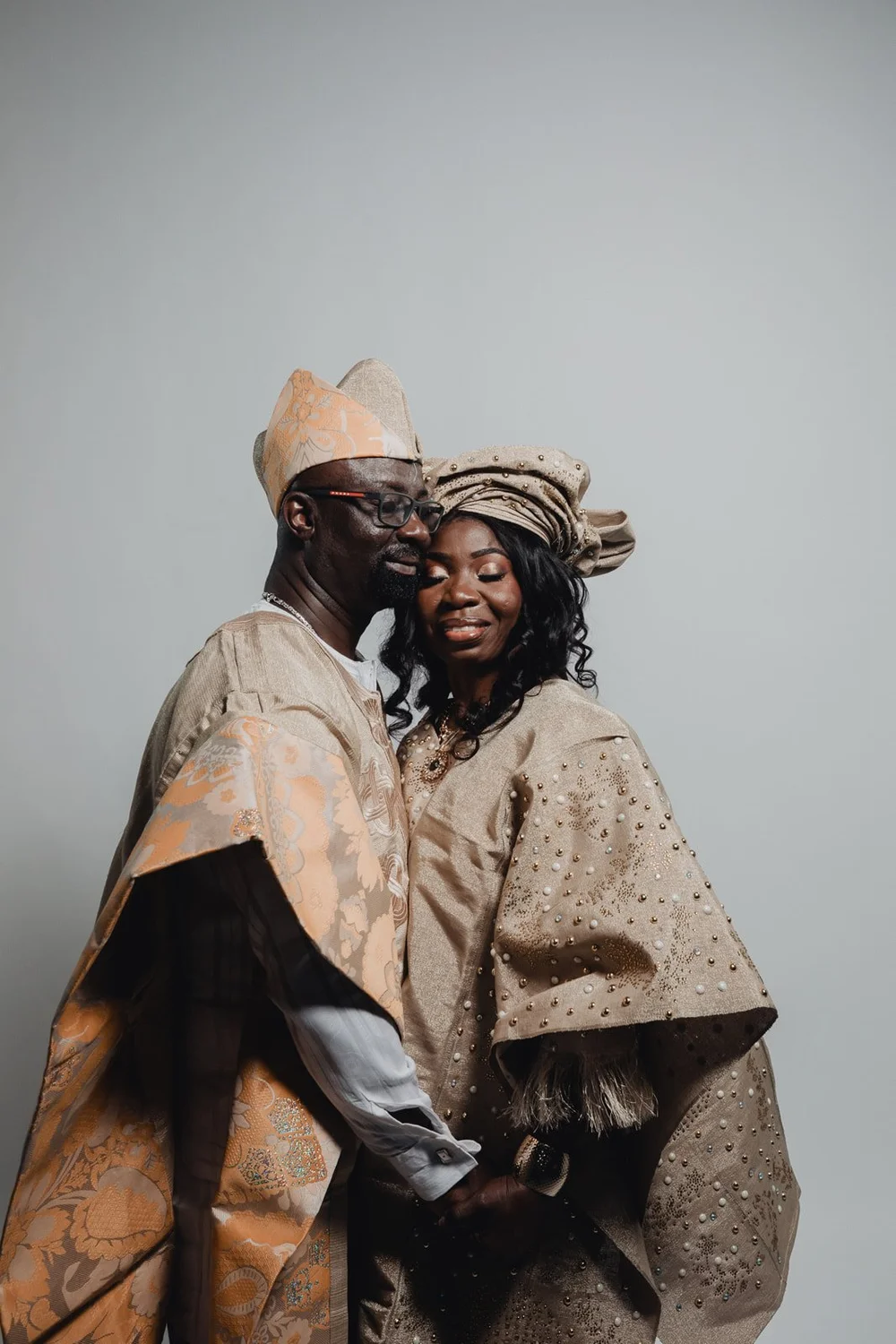 Groom leaning his cheek against his bride’s gele, both in cream and peach aso ebi