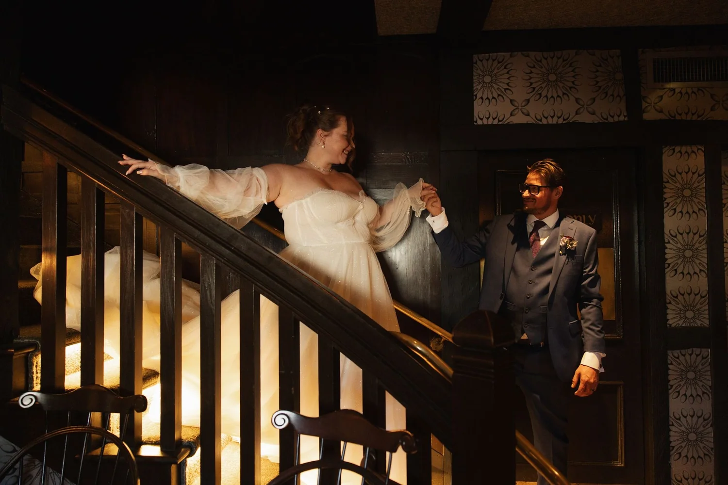 Bride at the dark wood staircase inside Five Crowns, lit warmly from below
