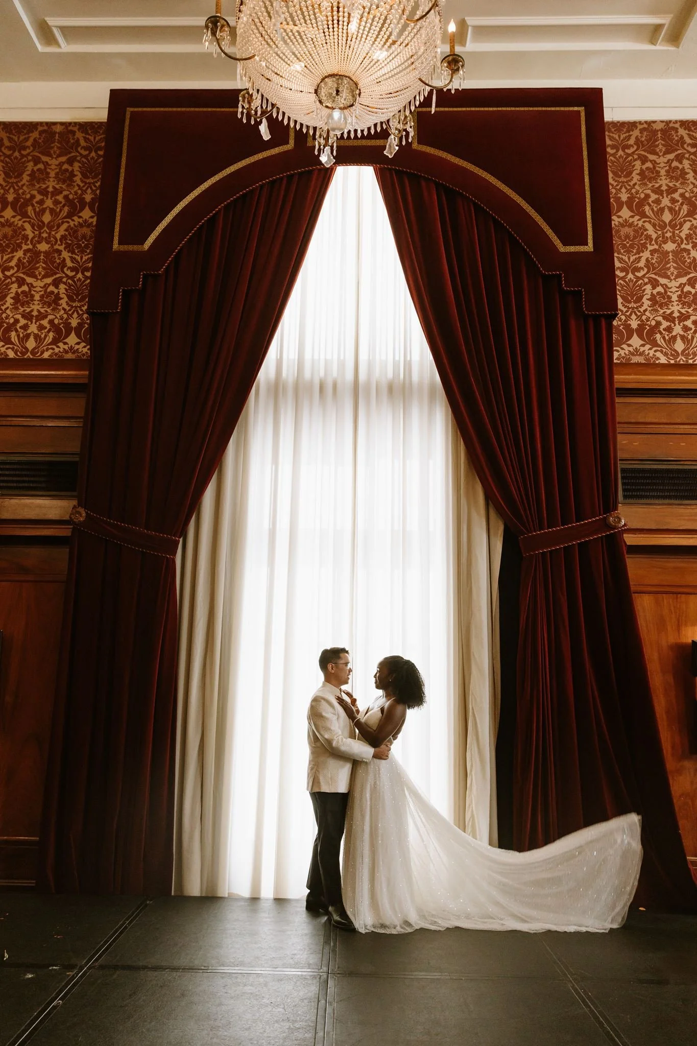 Couple framed by heavy burgundy velvet drapes and a crystal chandelier in a downtown Los Angeles lounge