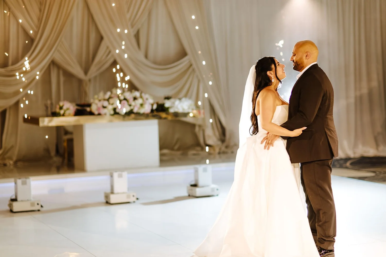 Couple embracing in front of the sweetheart table and draped wall at Glenoaks Ballroom