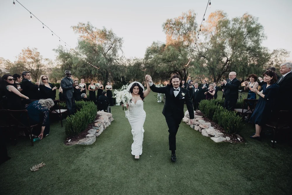 Bride and groom walking back down the grass aisle at Terra in Murrieta as guests applaud beneath bistro lights