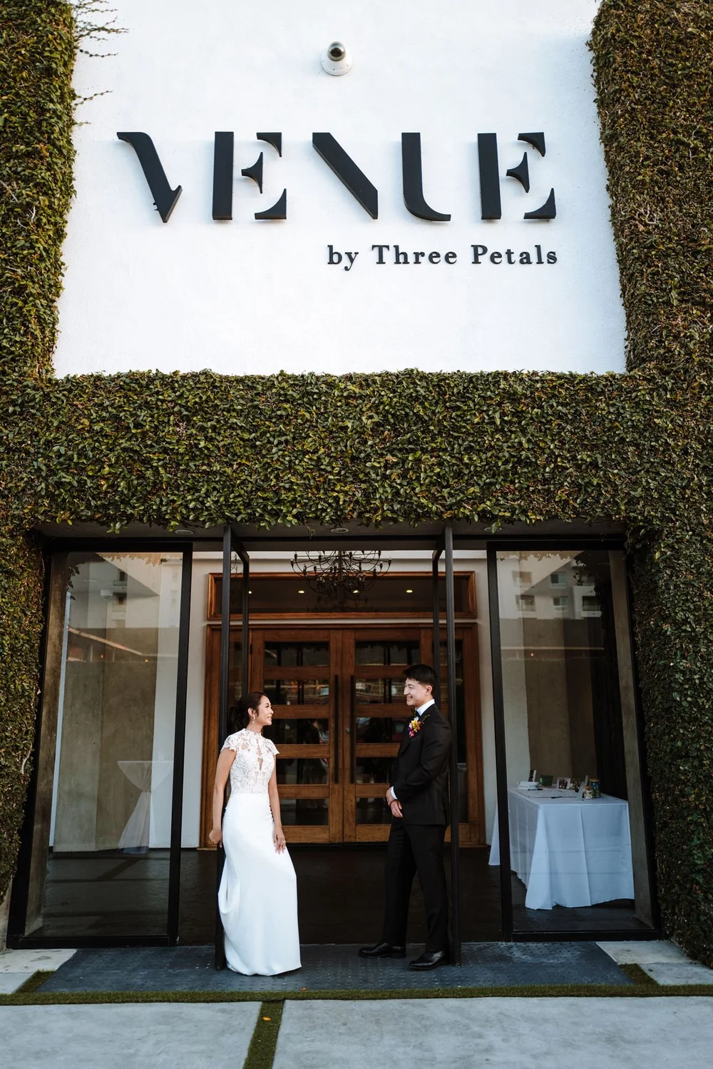 The green-wall entrance of Venue by Three Petals in Huntington Beach, with the couple at the doors