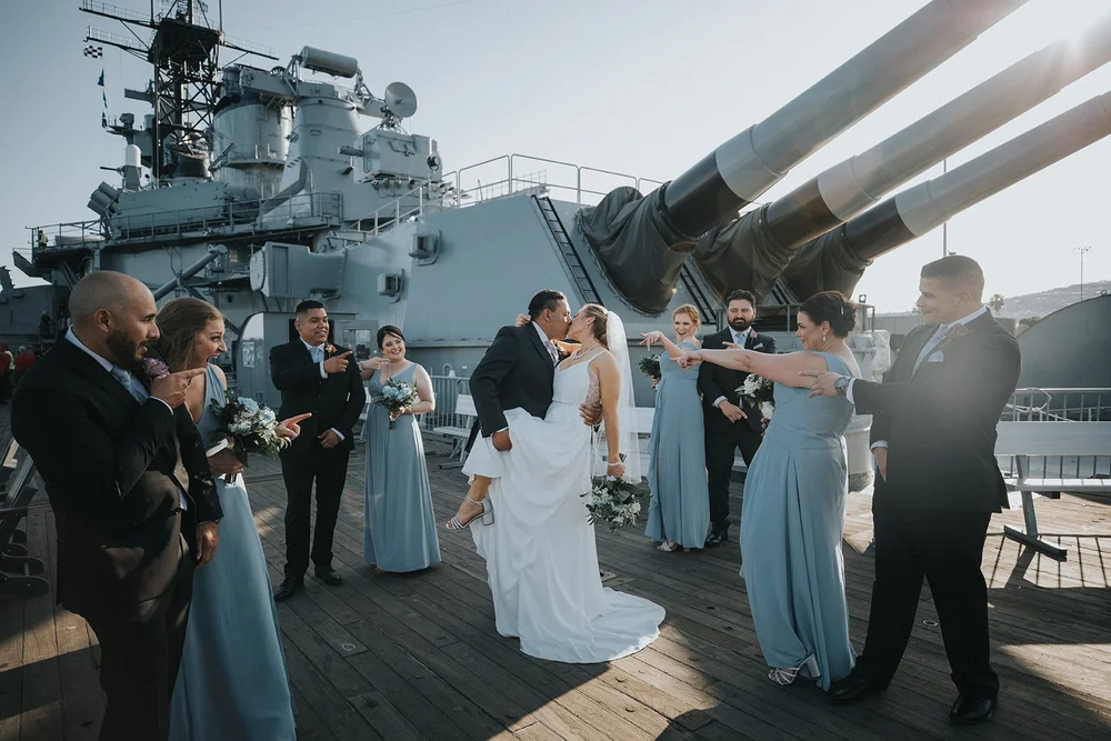 Couple kissing on deck surrounded by their wedding party in dusty blue